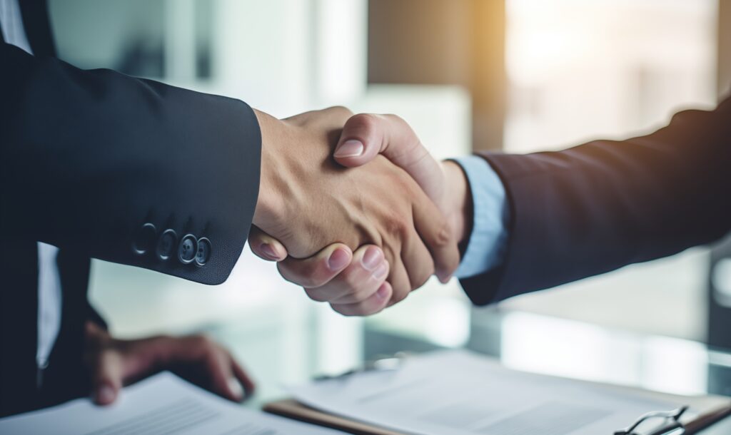 Two lawyers in suits shake hands over legal documents in an office setting.